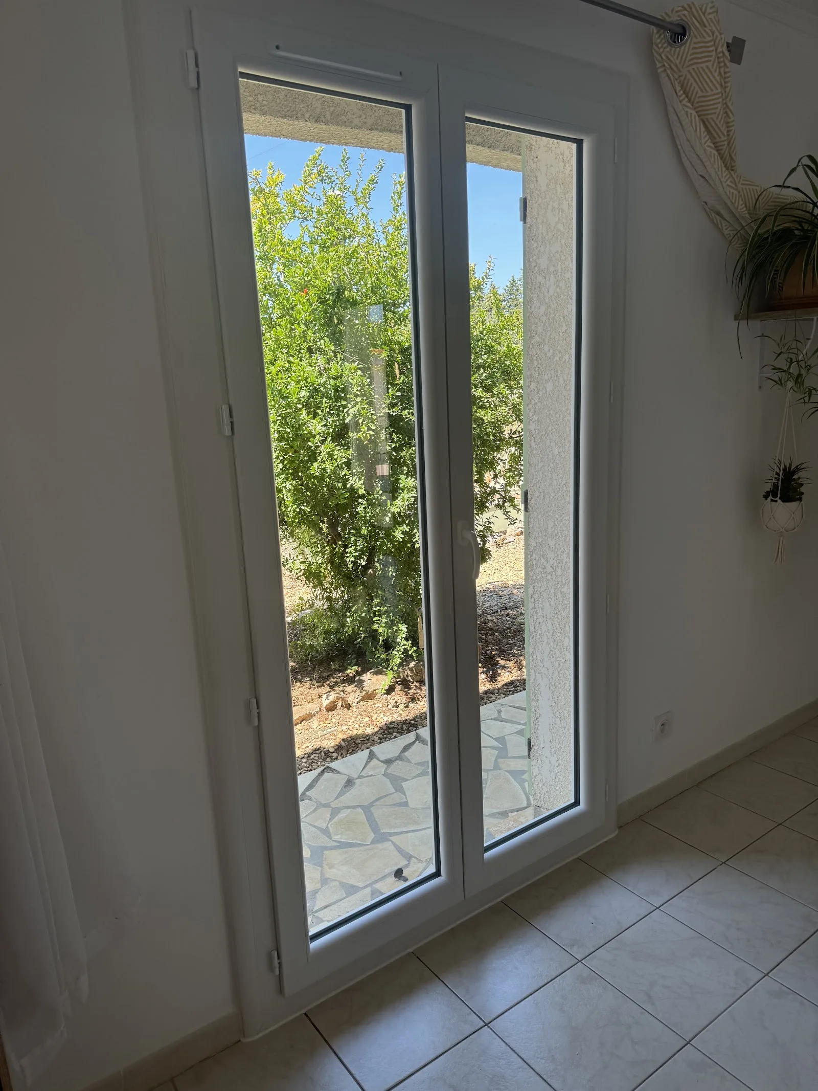 Porte-fenêtre PVC blanche ouvrant sur un jardin d'oliviers
