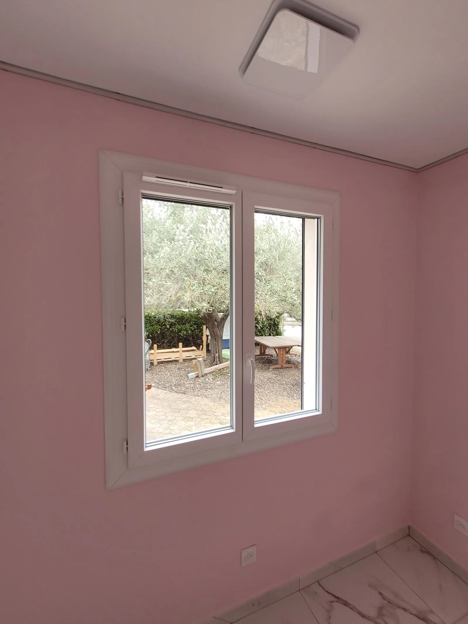 Fenêtre PVC blanche dans une pièce, vue sur un olivier